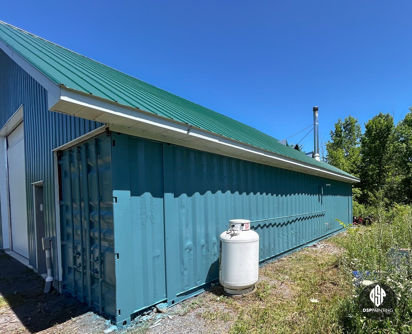 The long side of the building after painting, the container’s corrugated steel teal below the green metal roof