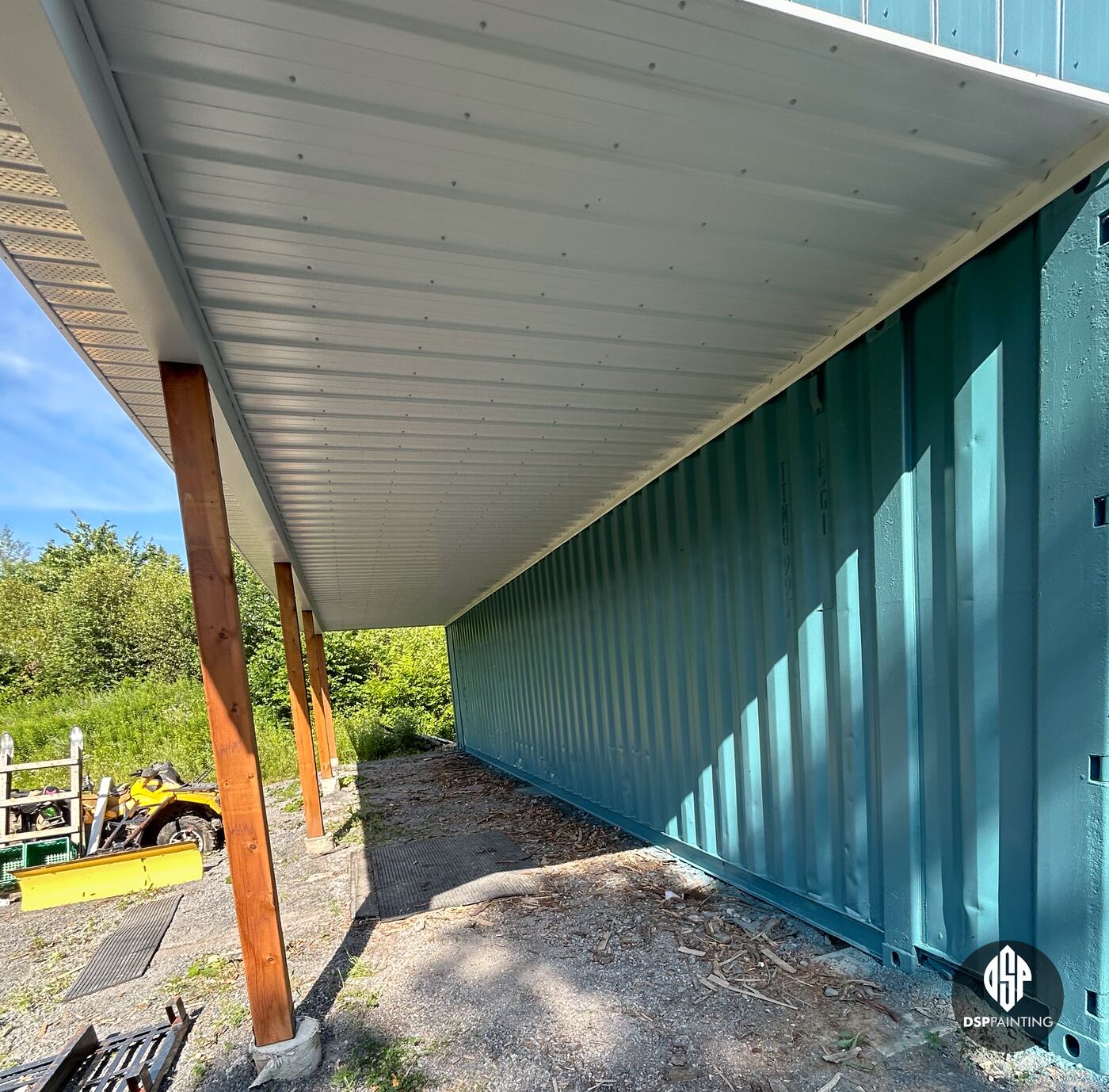 Under the overhang after painting, the container’s corrugated side teal along its full length