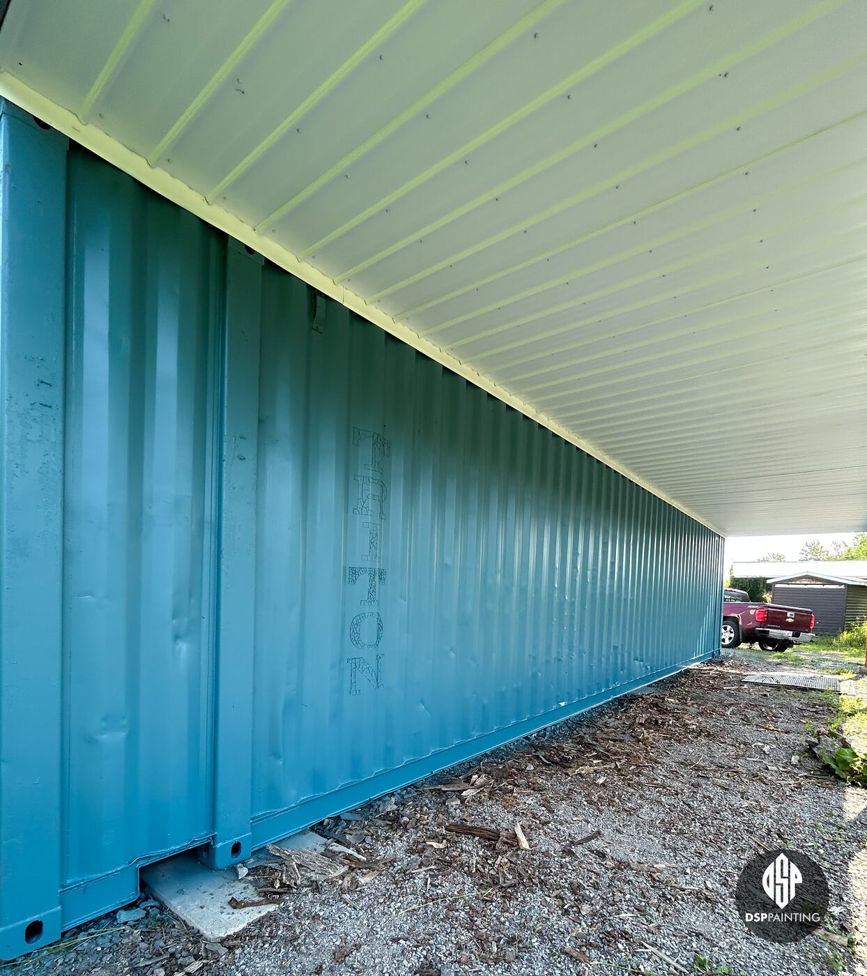 The container’s side after painting, teal over the old lettering, beneath the white steel overhang